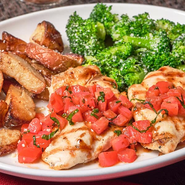 Closeup of Bertucci's Chicken Bruschetta Roma tomato bruschetta mix, shaved Asiago & balsamic glaze. Served with rosemary roasted potatoes & broccoli