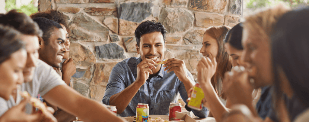 A group of people sitting at a table outdoors smiling and eating Bertucci's pizza together
