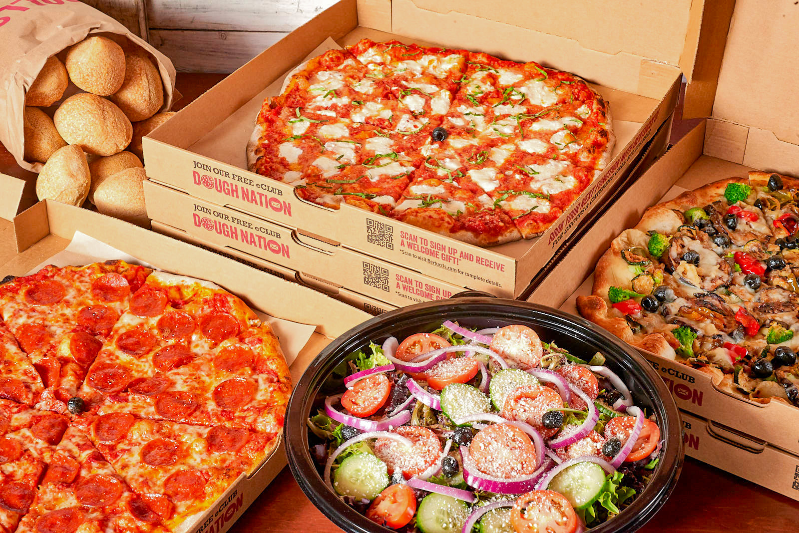 A display of three catered pizzas with a salad and rolls.