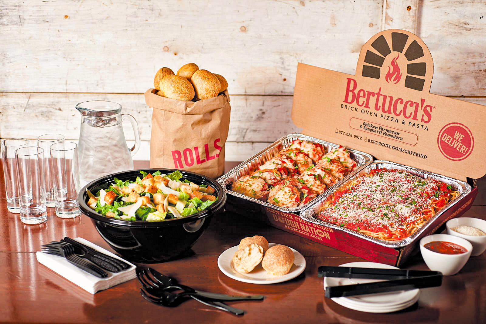 Chicken Parmesan and Spaghetti in catering trays beside Bertucci's famous rolls and a huge bowl of salad.